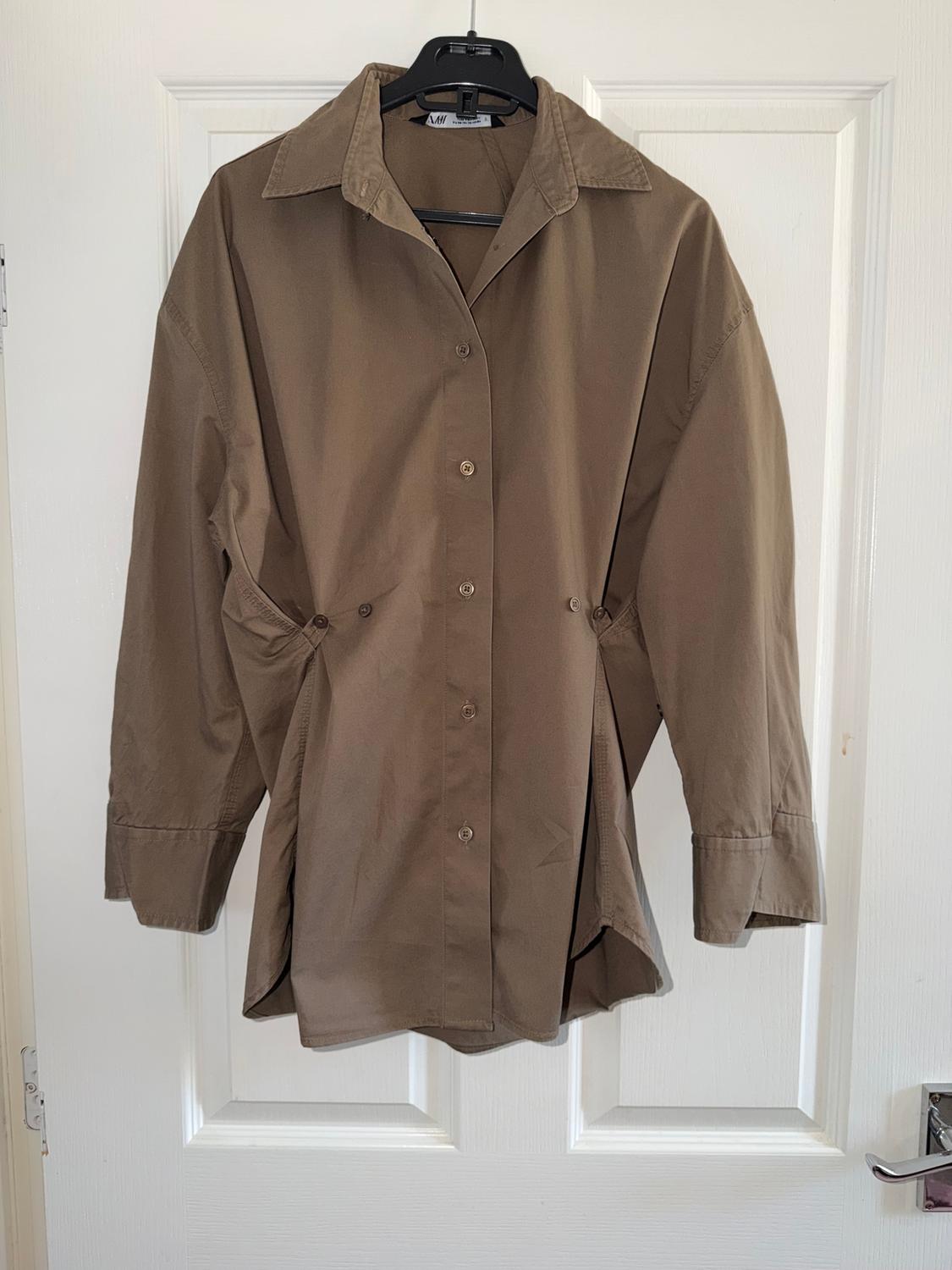 Brown long-sleeved shirt hanging on a black hanger over a white door.