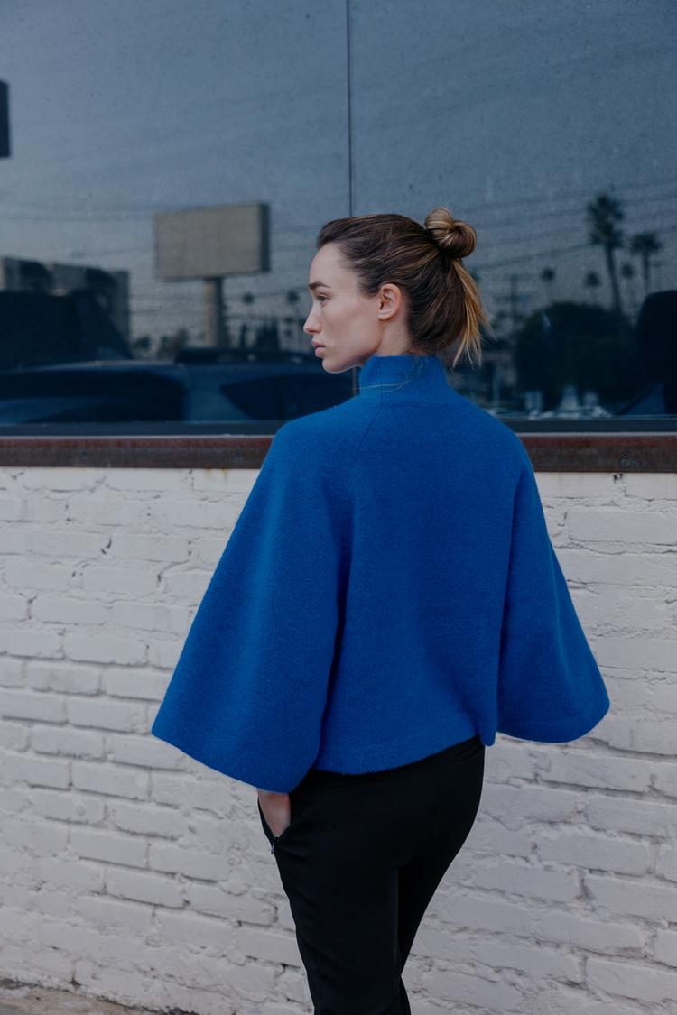 Sada modrého svetru s širokými rukávy a černých kalhot.