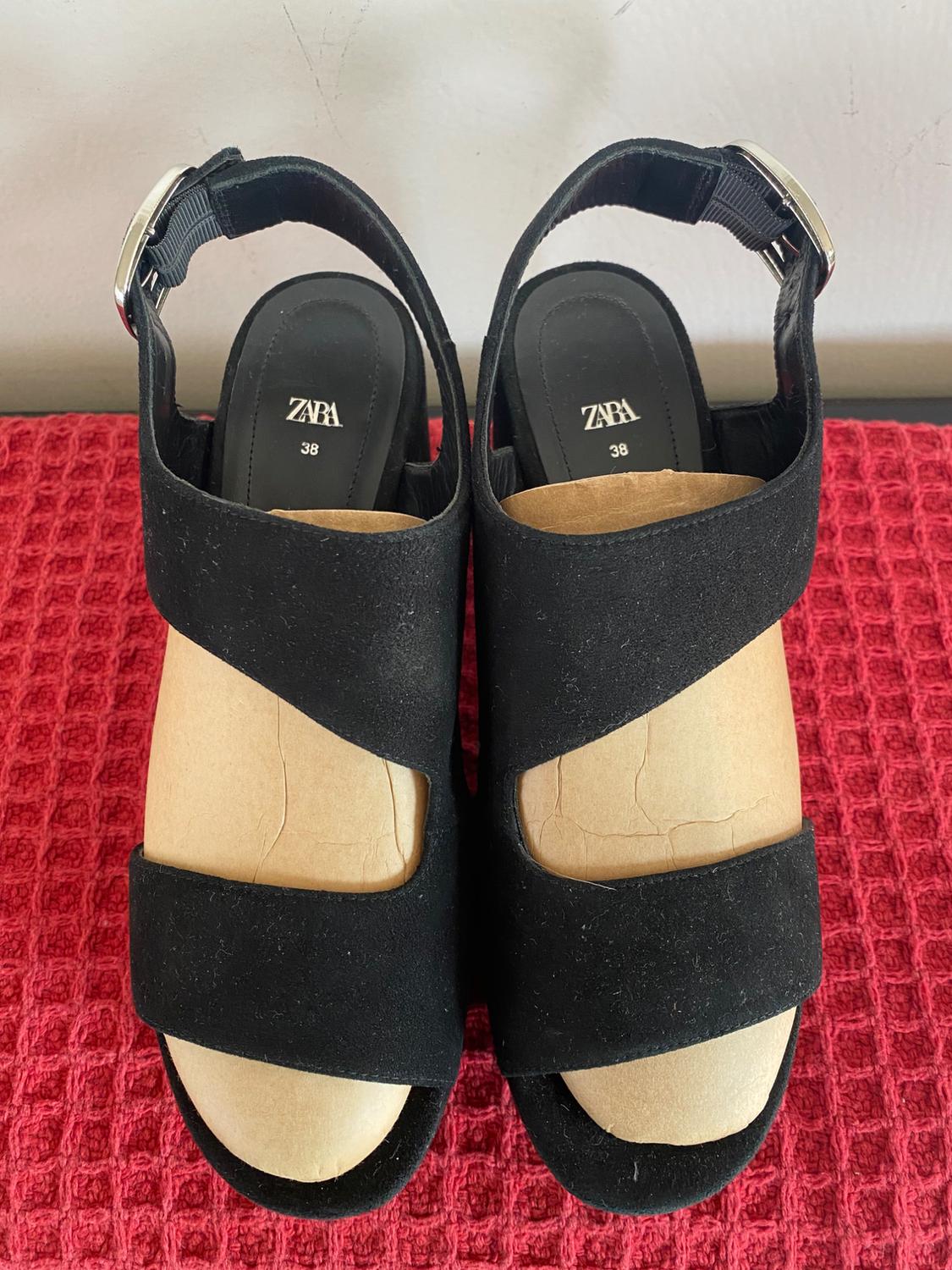 Black platform sandals with buckle, Zara brand, on a textured red surface. Size 38 visible on the insole.