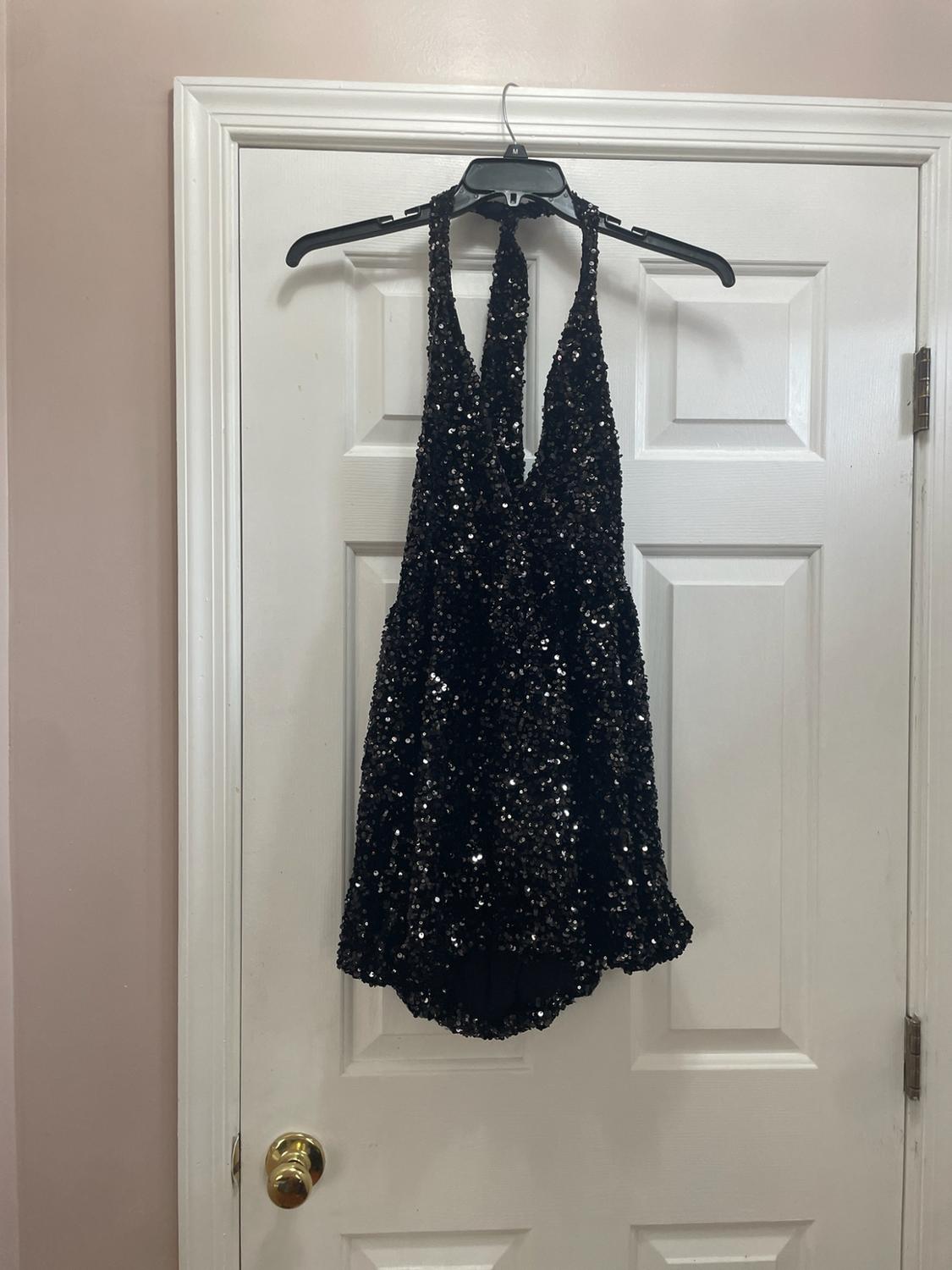 Short black sequin halter dress hanging on a hanger over a white door in a home setting.
