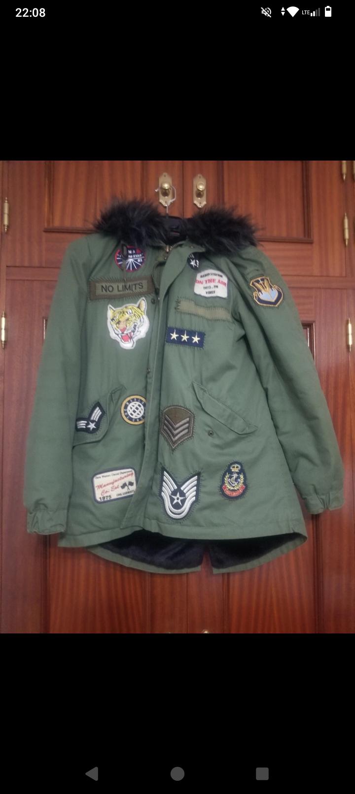 Green jacket with assorted patches and black fur collar. Visible text: "NO LIMITS". Wooden background.