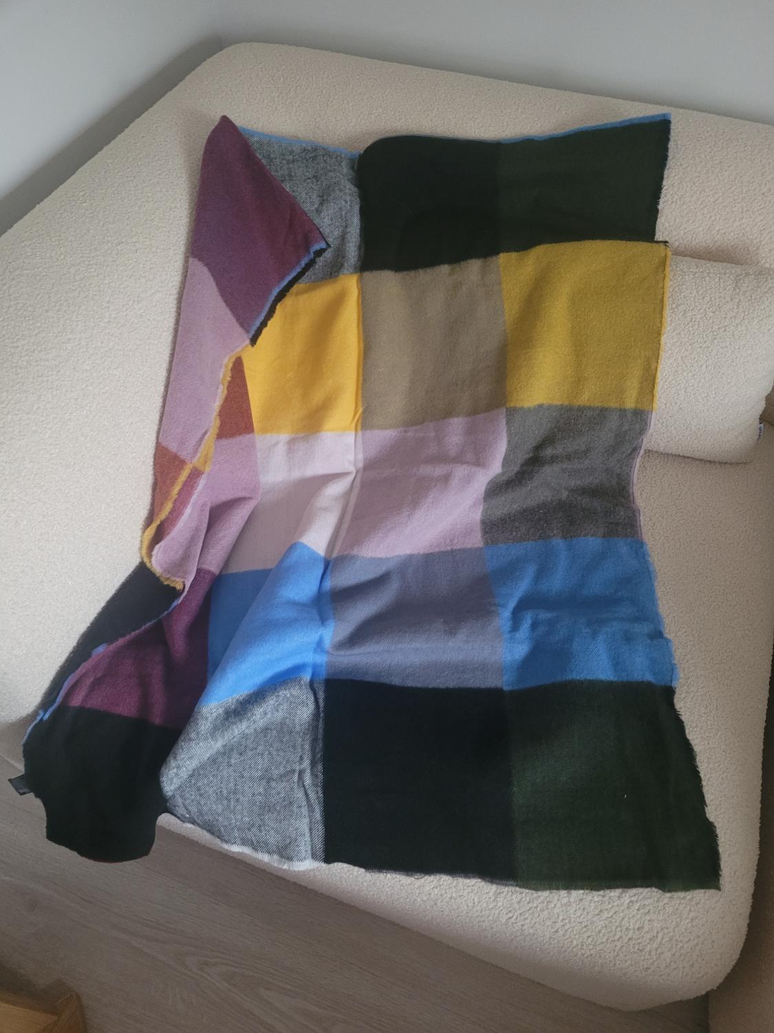 Multicoloured checked throw in shades of blue, yellow, green, and purple, draped over a beige sofa in the corner of the room.