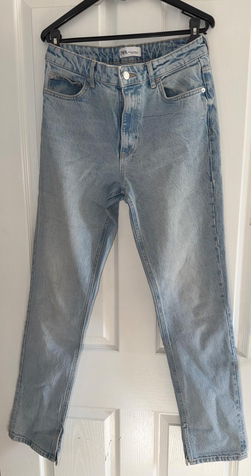 Light blue jeans hanging on a black hanger over a white door. Visible tag: "Zara".