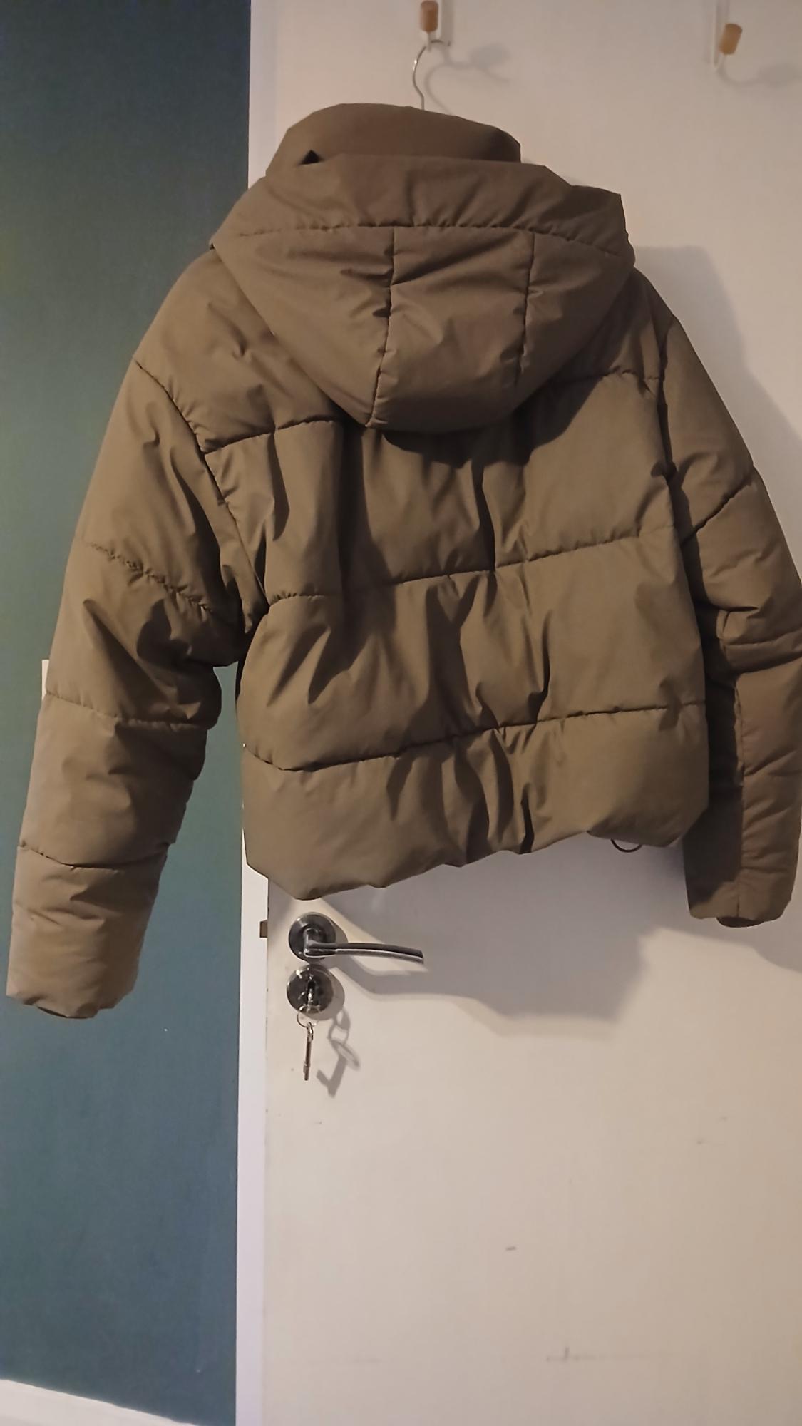 Brown quilted jacket hanging on a white door with a blue wall in the background. The door has a key lock.