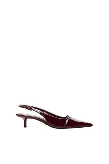 Glossy burgundy low-heeled slingback shoe with a pointed toe and metallic detailing at the front, against a white background.