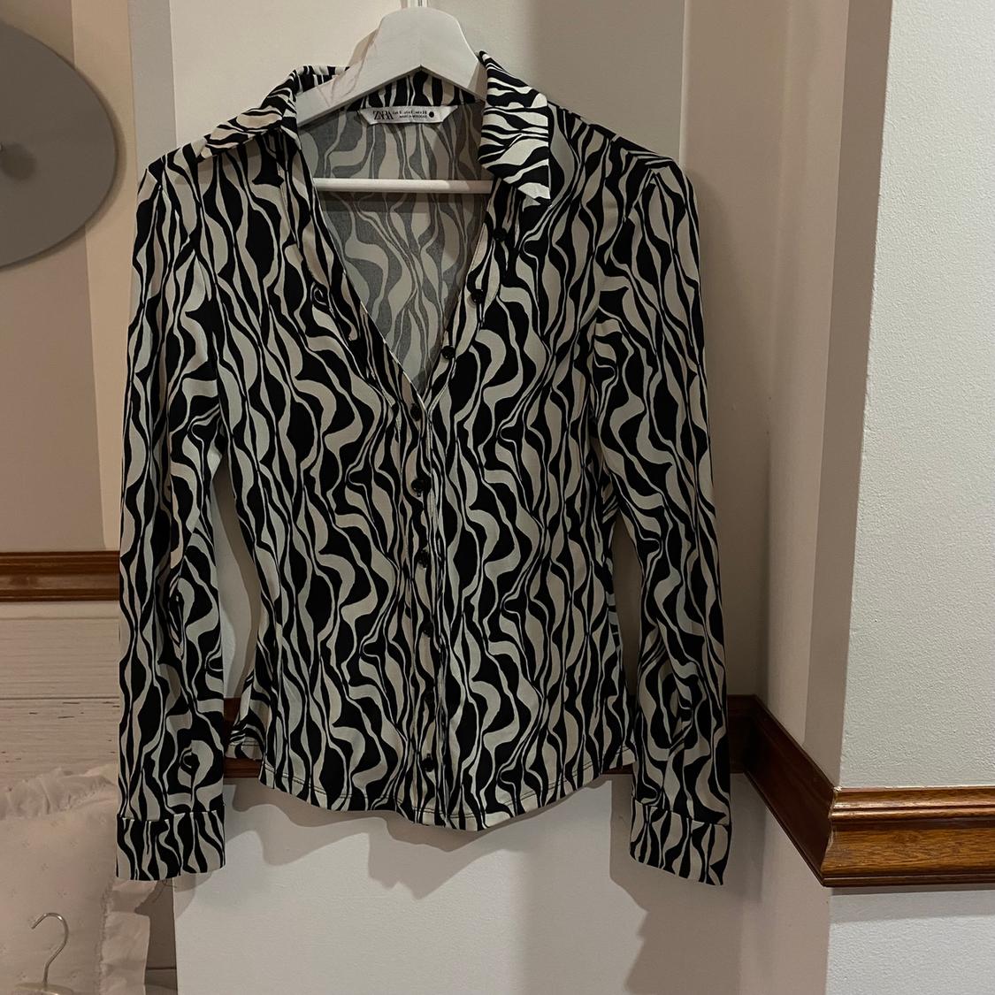 Black and white wavy print long-sleeved shirt hanging on a white hanger against a light wall.