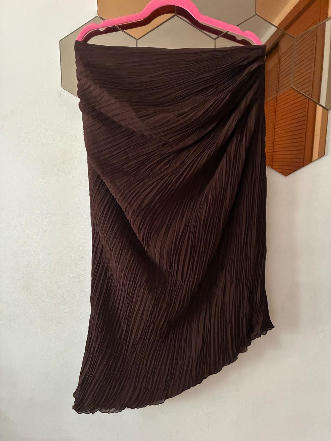 Brown pleated skirt hanging on a pink hanger, reflected in a hexagonal mirror on the white wall.