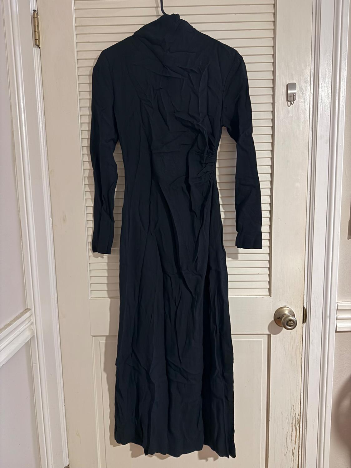 Long-sleeved black dress hanging on a white panelled door. The fabric is creased, creating a textured effect.