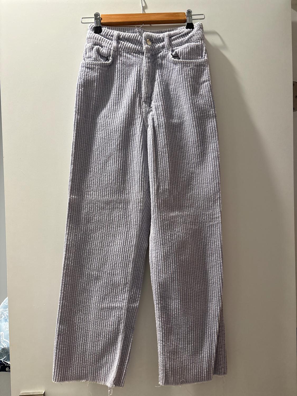 Light gray corduroy pants hanging on a wooden hanger against a white background. Straight-leg and high-waisted design.