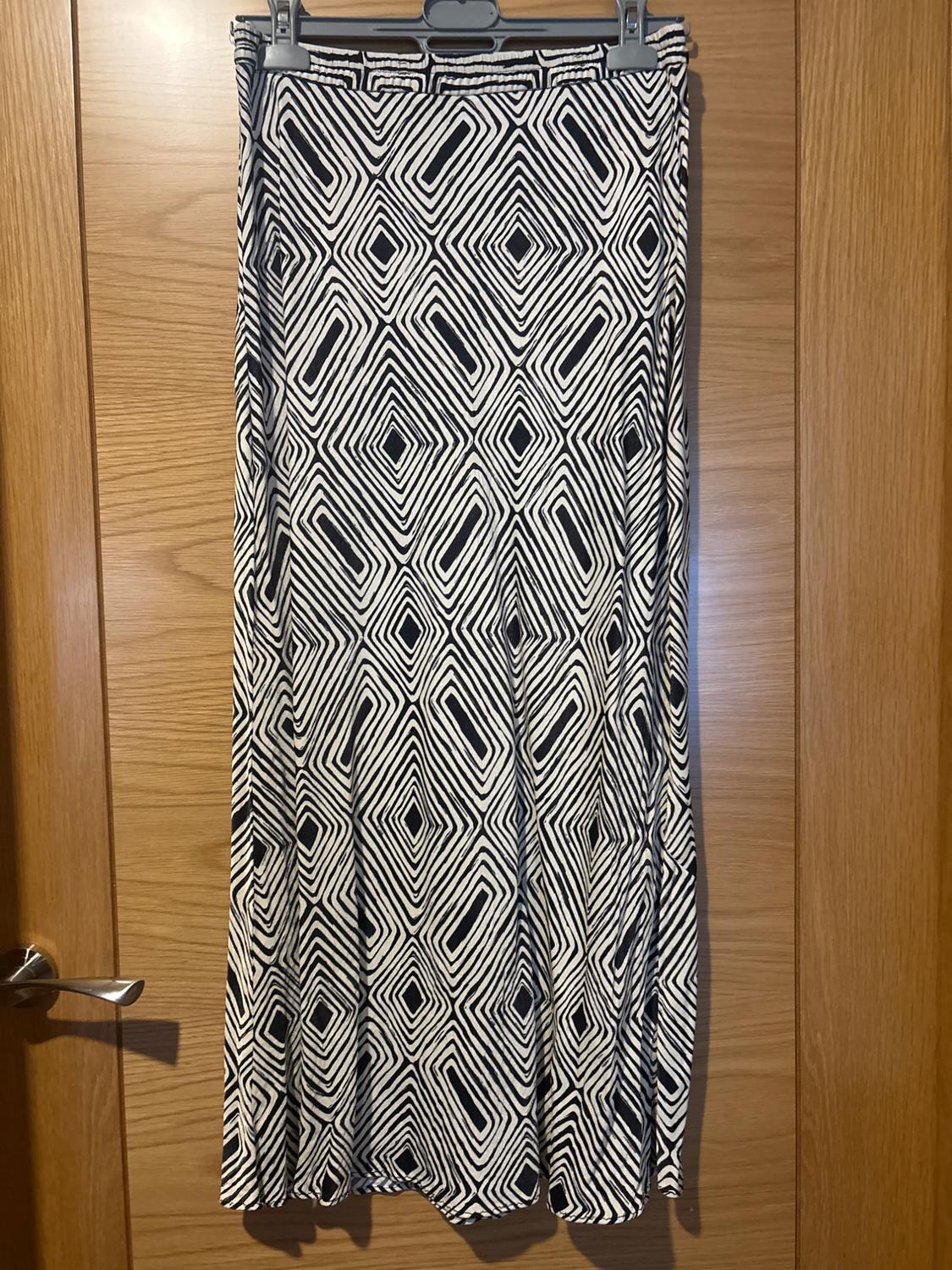 Black and white diamond-patterned maxi skirt, hanging on a hanger in front of a wooden door.