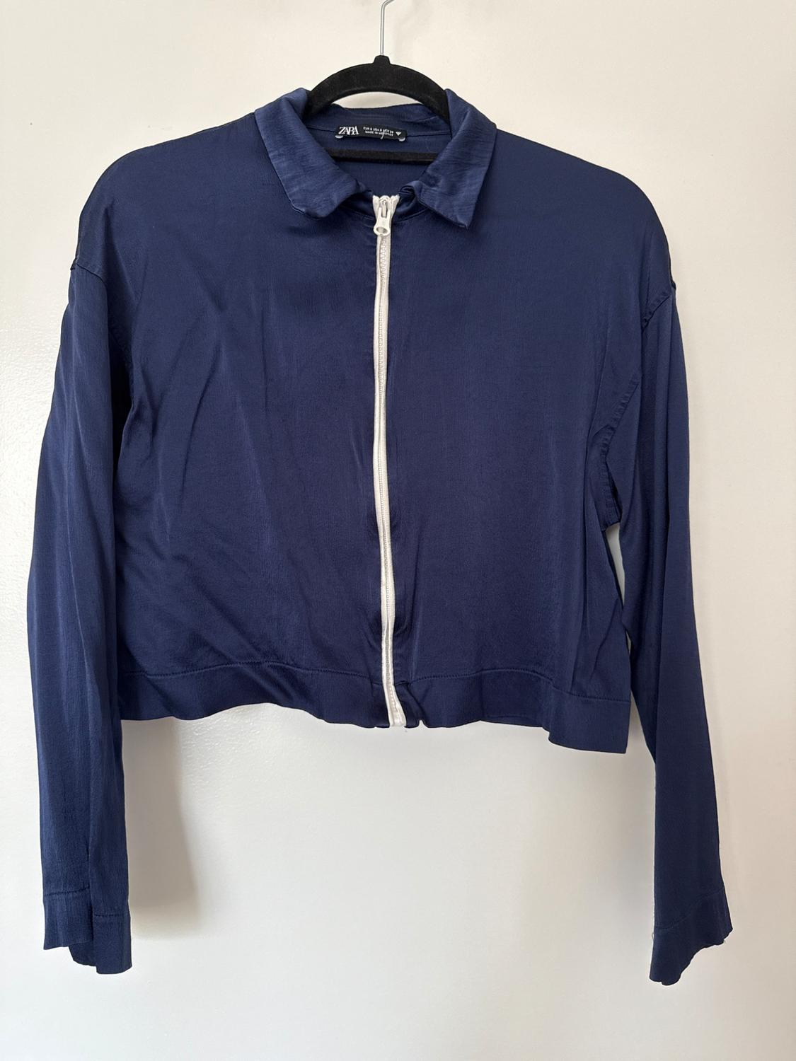 Navy blue long-sleeved jacket with a collar and white zip, hanging on a black hanger against a white background. ZARA label visible.