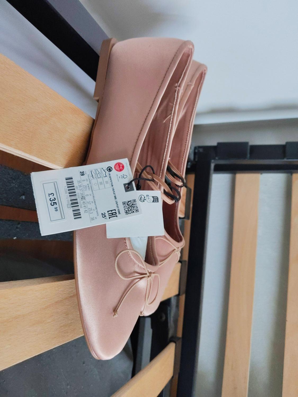 Pink ballet flats with a bow on wooden slats. Label: £35.99 39 EAC 218-FLAT SHOE 218-FLAT SHOE.
