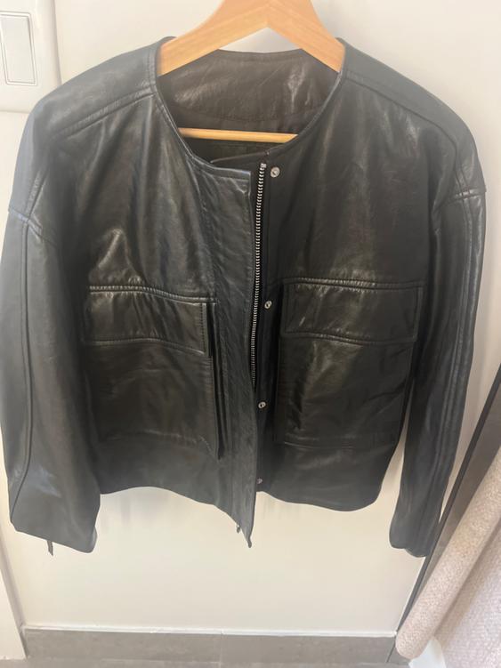 Black leather jacket hanging on a wooden hanger, with zipper and front pockets, on a white background.