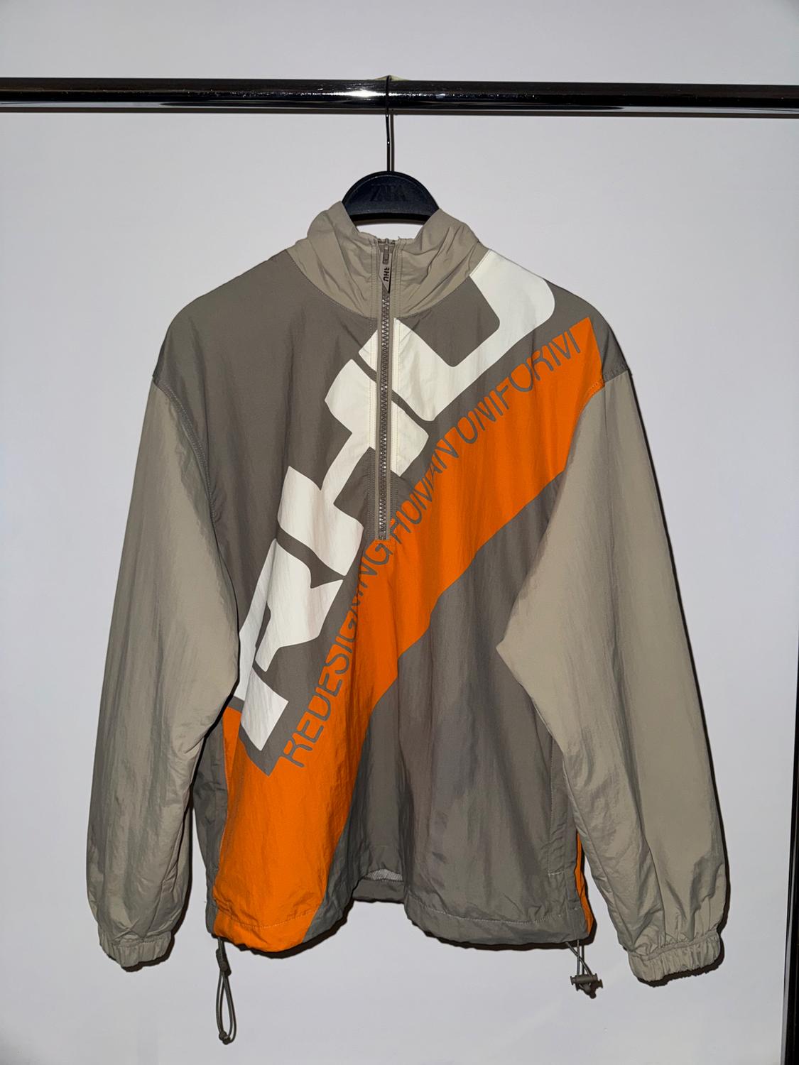 Jacket hanging on hanger, with design in grey, white, and orange. Visible text: "REDESIGN YOUR UNIFORM". White background.