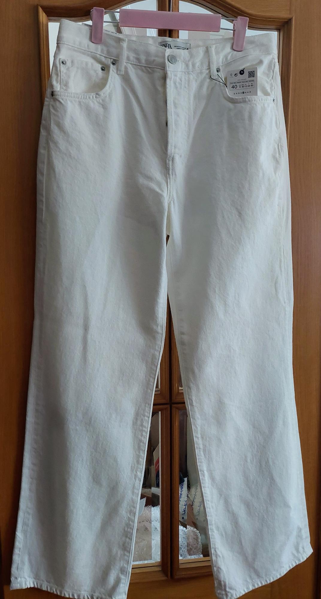 Front view of white trousers with front pockets and visible label.