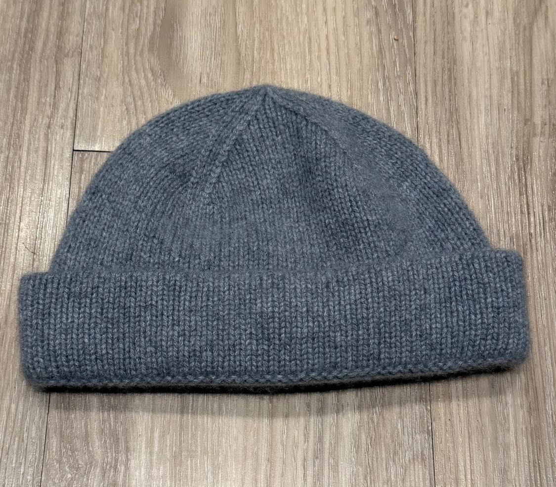 Grey knitted hat on a light wooden floor. The knit is thick and has a wide hem at the bottom.