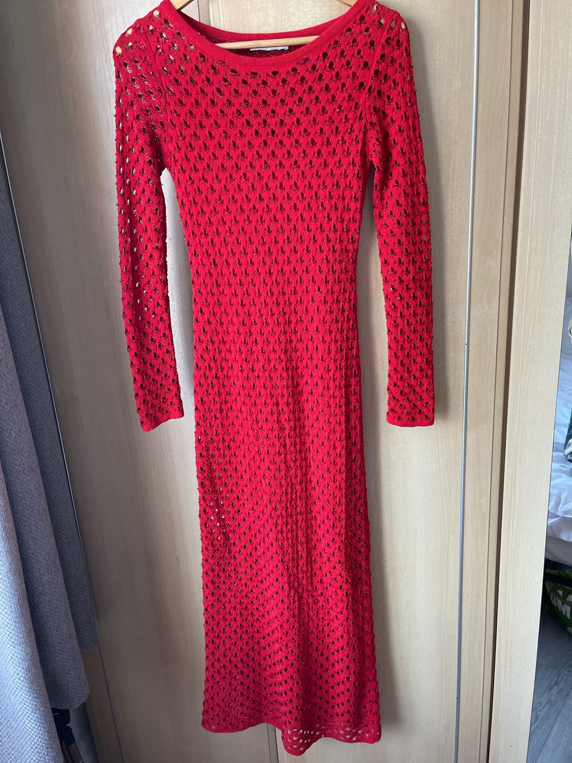 Red open-knit dress with long sleeves, hanging on a wooden hanger over a light wood wardrobe door.