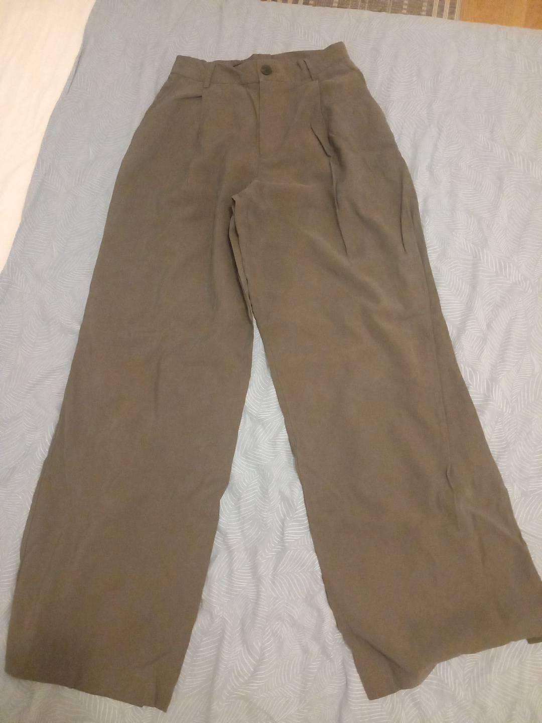 Brown wide-leg trousers with pleats and a button, laid out on a light blue sheet. Casual and relaxed style.