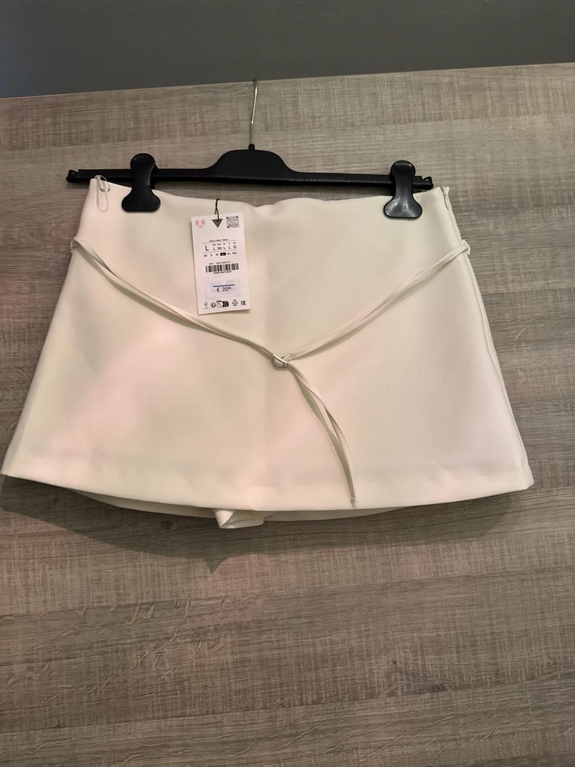 White skort with drawstring detail on a black hanger against a wooden background. Tag with the text L L 30 L L G € 25.95.