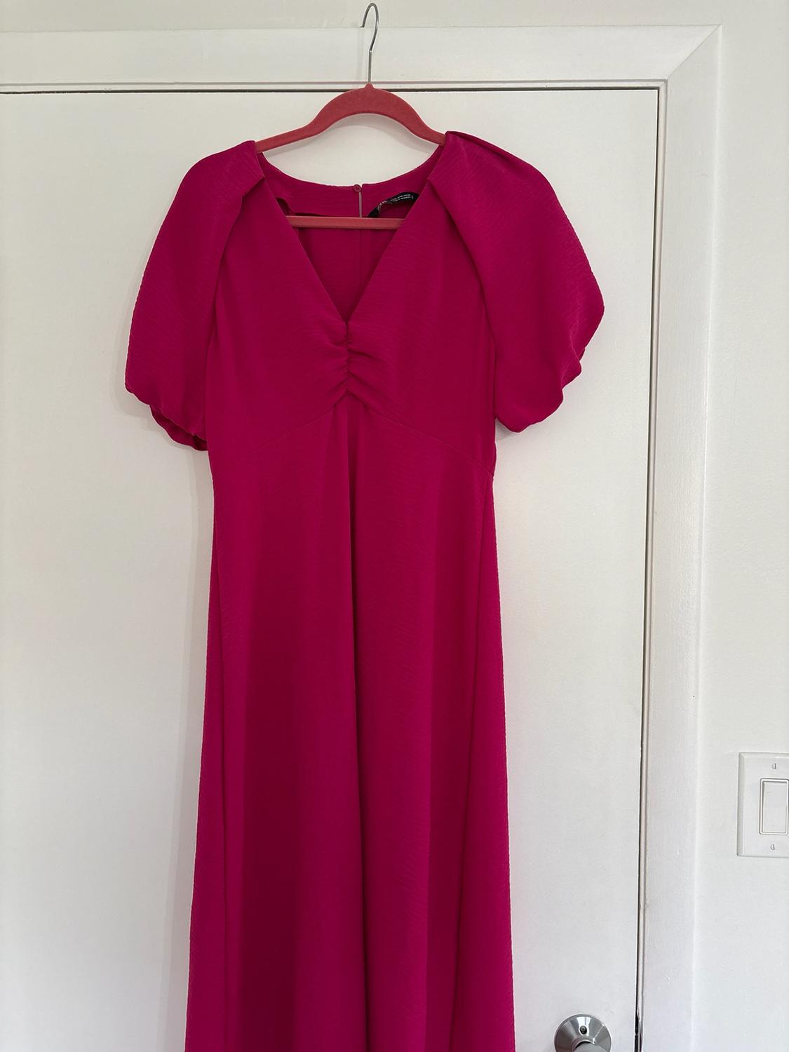 Fuchsia short-sleeved puff-sleeve dress with a gathered V-neck, hanging on a pink hanger on a white interior door.