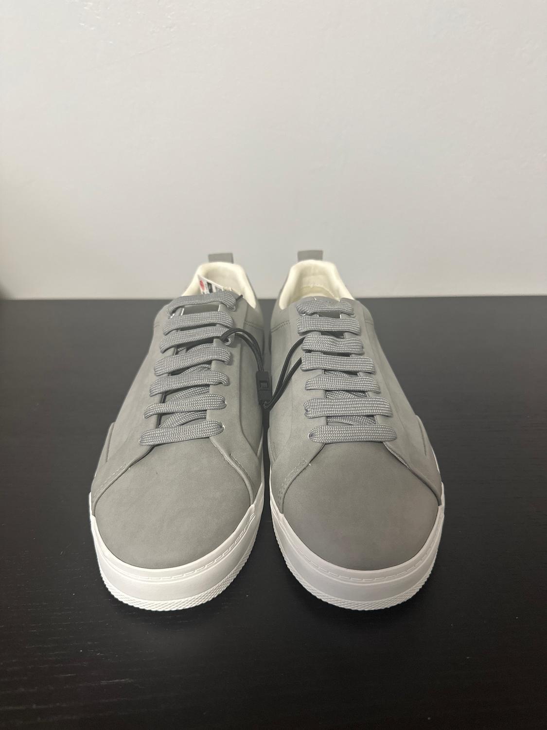 Grey suede trainers with grey laces on a black surface. White sole and white background.