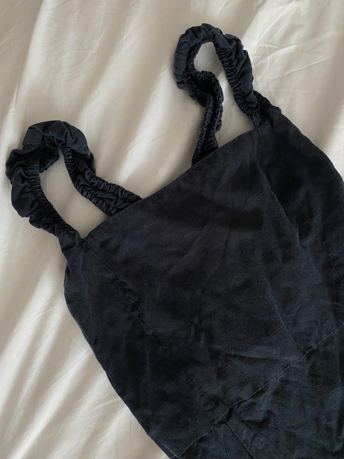 Close-up of a black top with ruched straps and a straight neckline on white sheets. Relaxed and minimalist composition.