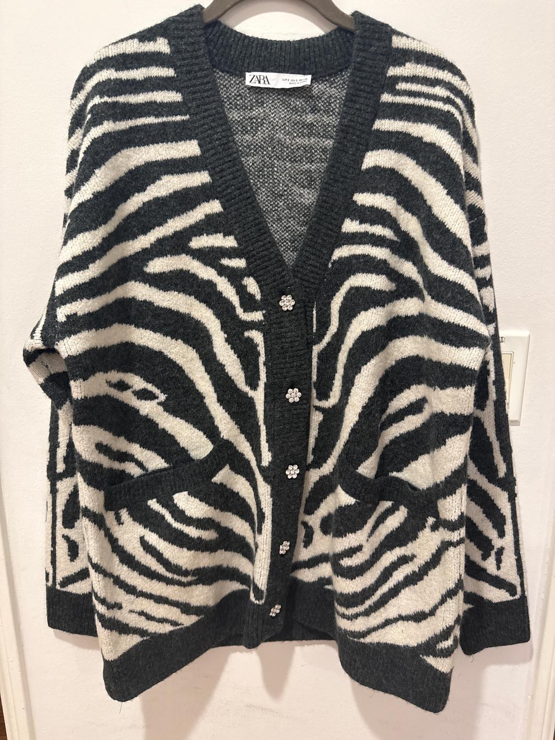 Black and white zebra print knitted cardigan with decorative buttons and front pockets. Visible tag: ZARA.