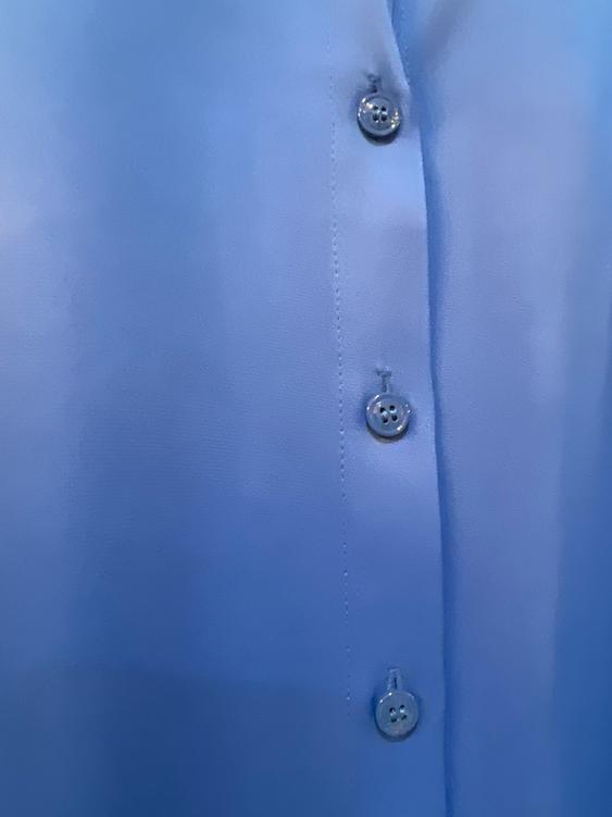 Detail of a blue shirt with visible buttons in the foreground. The fabric has a smooth and shiny finish.