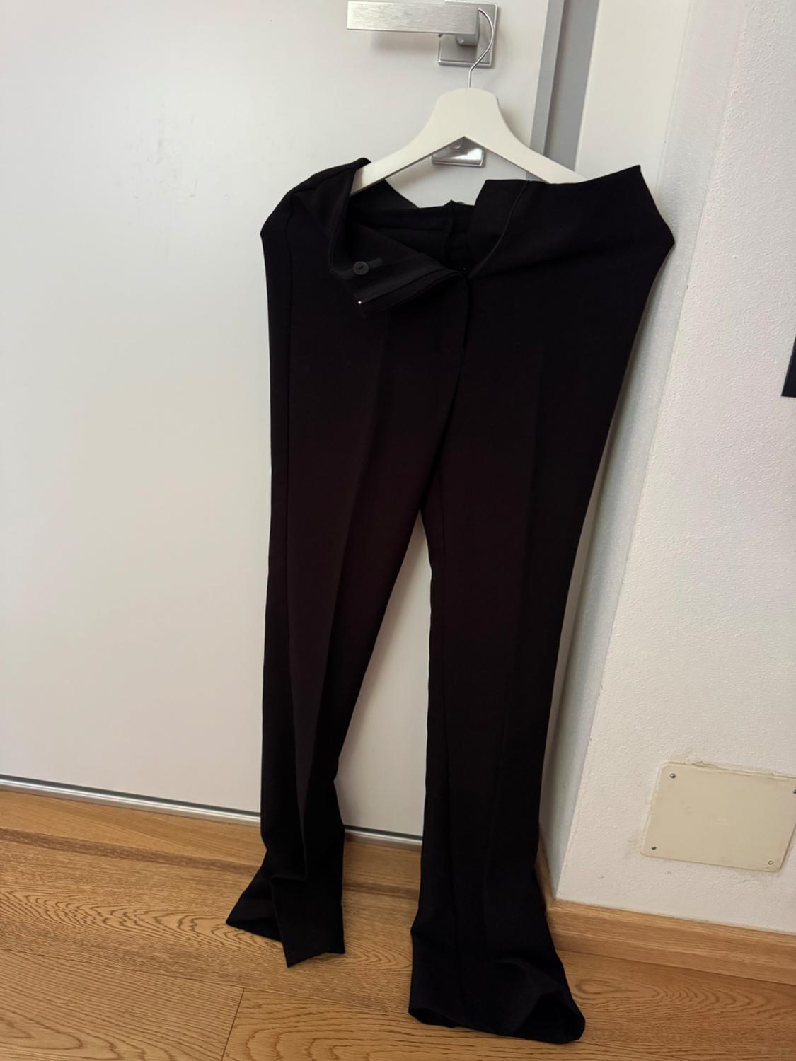 Black trousers hanging on a white hanger over a white door, with light wooden flooring visible at the bottom.