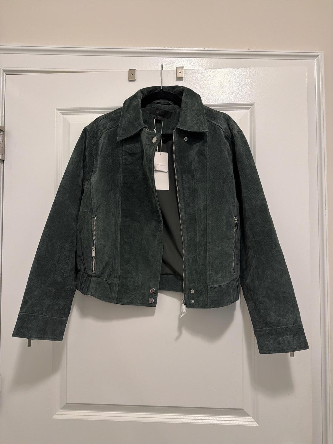 Dark green textured jacket with a zipper and pockets, hanging on a white door. Casual style and relaxed vibe.