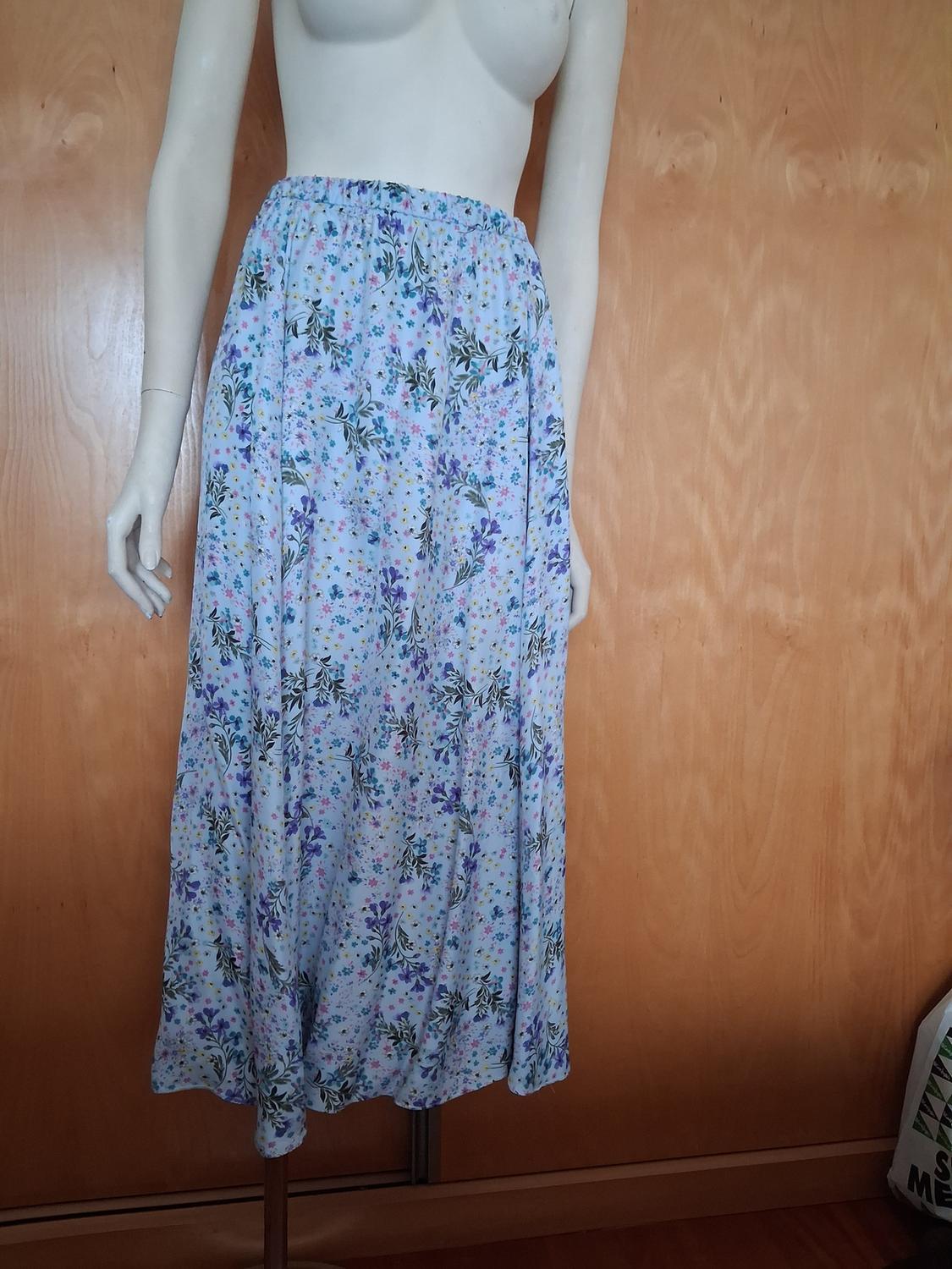 Mannequin with a long floral skirt in shades of blue and lilac against a light wooden background.