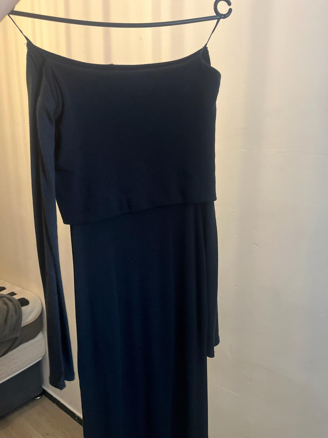 Dark ribbed dress with long sleeves and a folded neckline, hanging on a black hanger against a light-coloured wall.
