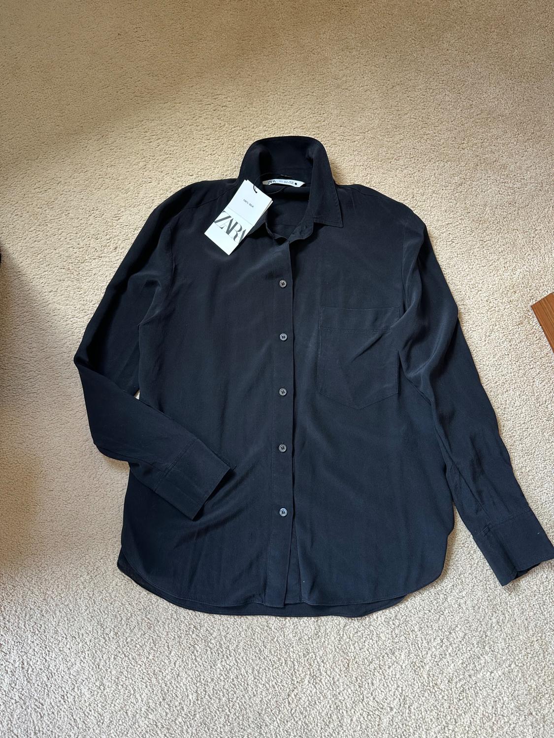 Black long-sleeved shirt with buttons and a pocket on a beige carpet. Label with the text ZARA and 100% SILK.
