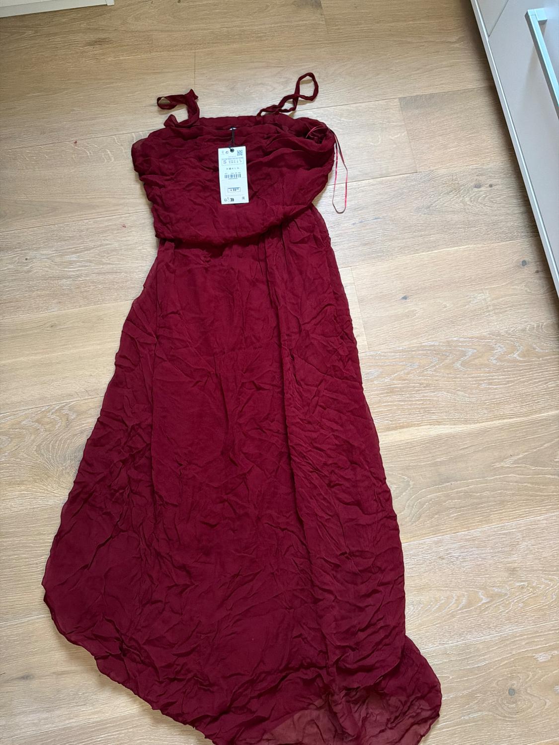 Wrinkled red maxi dress with thin straps on a light wooden floor. Visible label on the top of the dress.