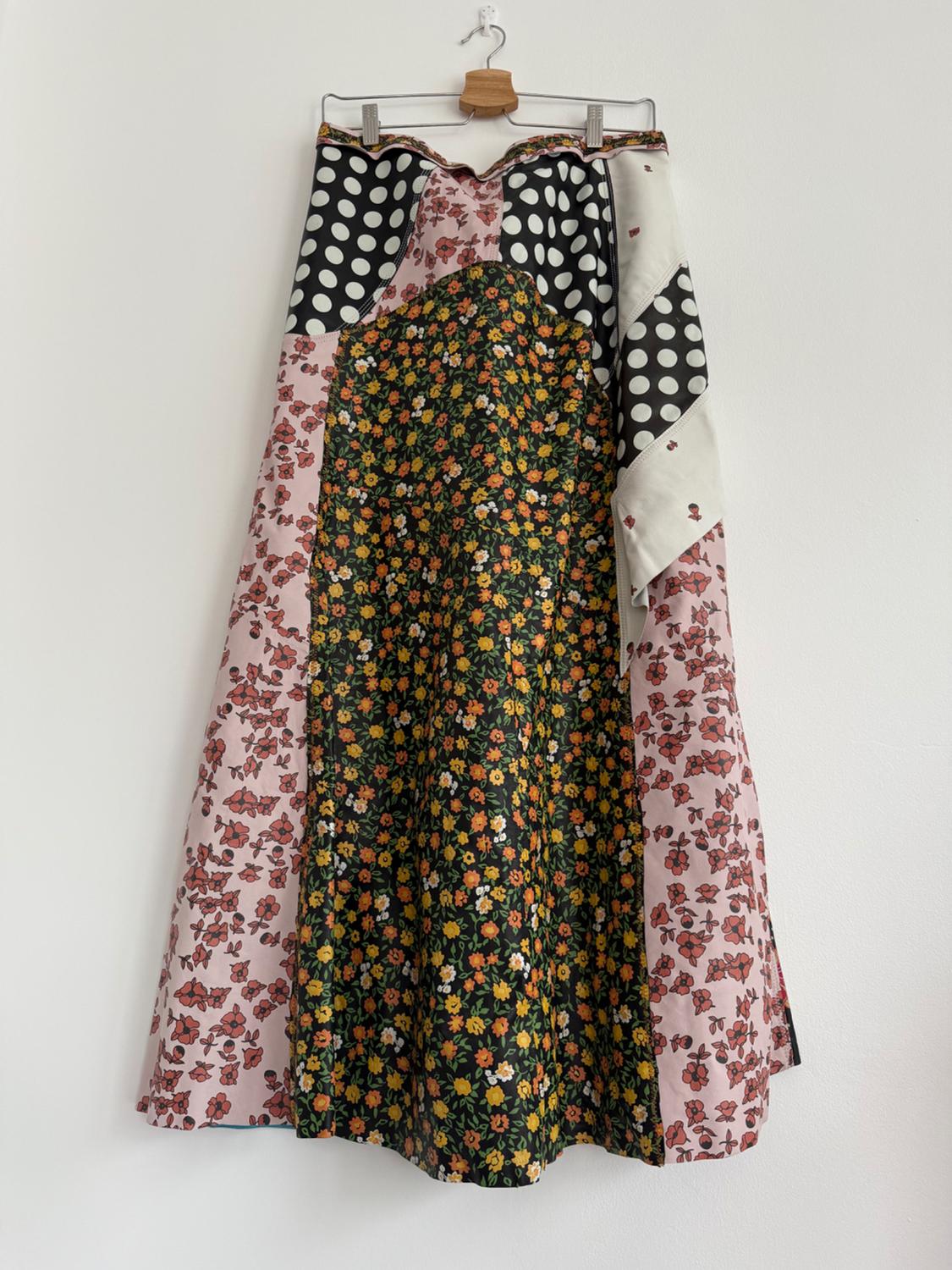 Hanging skirt with patchwork design of flowers and polka dots in black, pink and green tones on a white background.