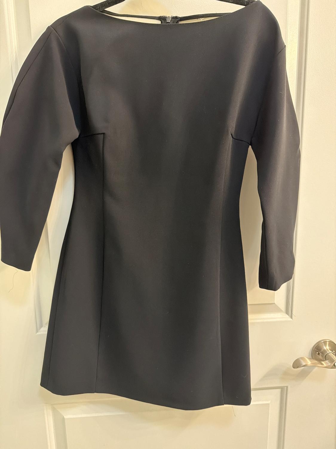 Long-sleeved black dress hanging on a white door. Simple and elegant design, ideal for formal occasions.