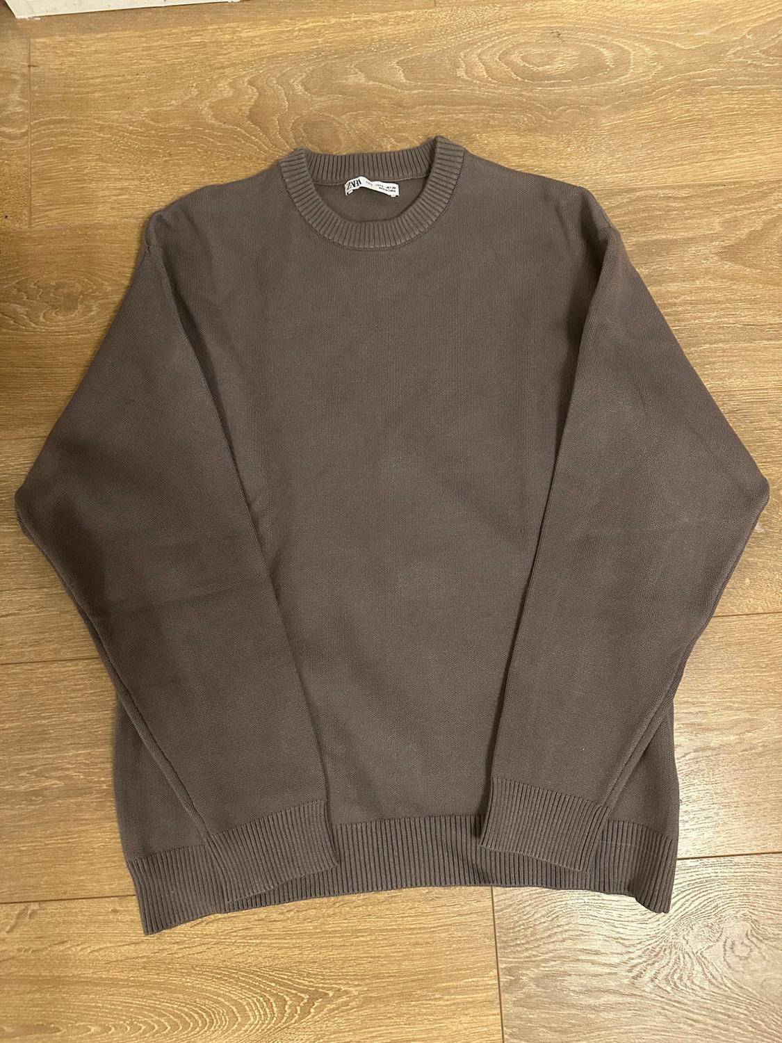 Brown crew neck, long-sleeved jumper on a light wooden floor. Visible label on the collar.