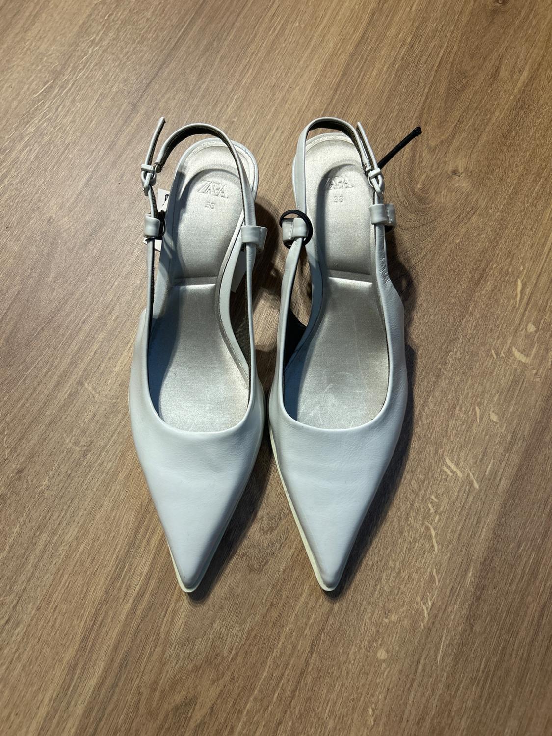 Slingback high heels in light grey on a wooden floor. Visible text: "ZARA 39".