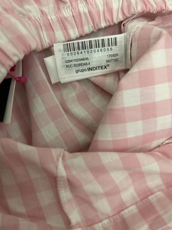 Clothing label with barcode on pink and white checked trousers. Visible text: "INDITEX group".