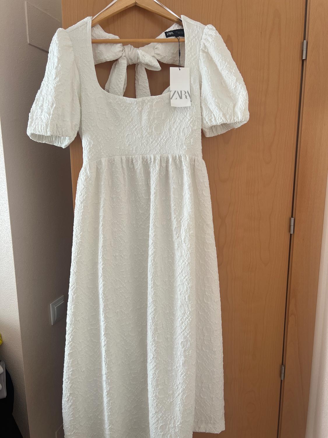 Front view of white dress with puff sleeves and a bow at the back.