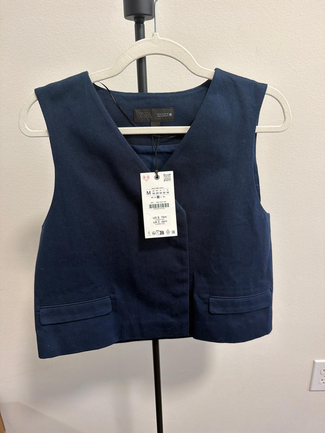 Dark blue vest on a hanger with a visible price tag, hanging on a black stand against a white background.