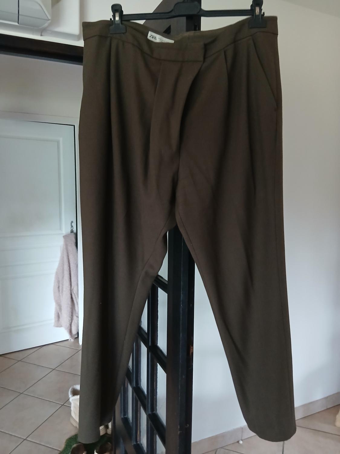 Brown trousers hanging on a black hanger in an interior with a tiled floor and a white door in the background.