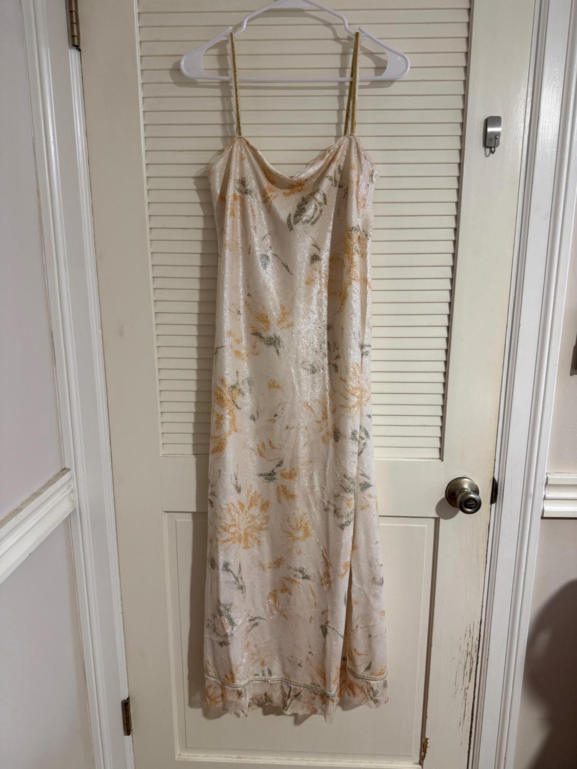Long dress with thin straps and a pastel floral print, hung on a white door with a shuttered background.