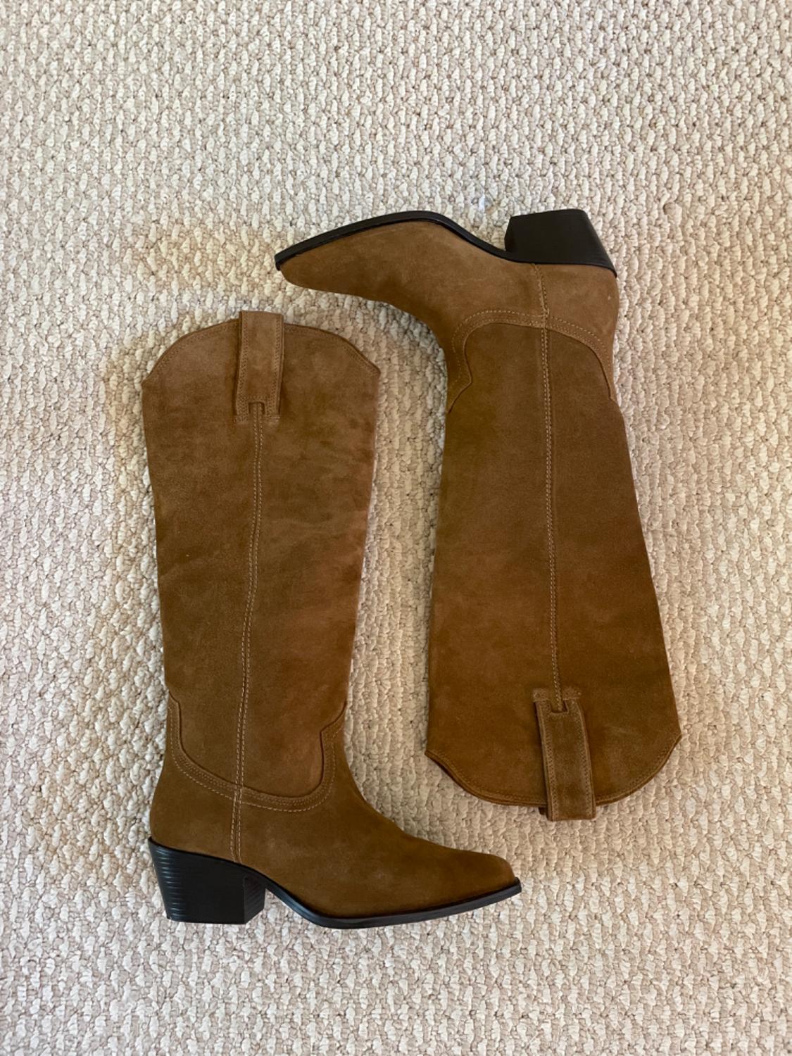 Brown suede knee-high boots with a low heel and pointed toe, placed on a light-textured rug.