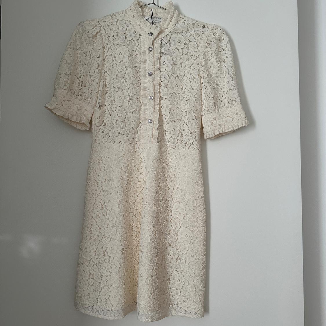 Cream white lace dress with short puff sleeves and front buttons, hanging on a white hanger.