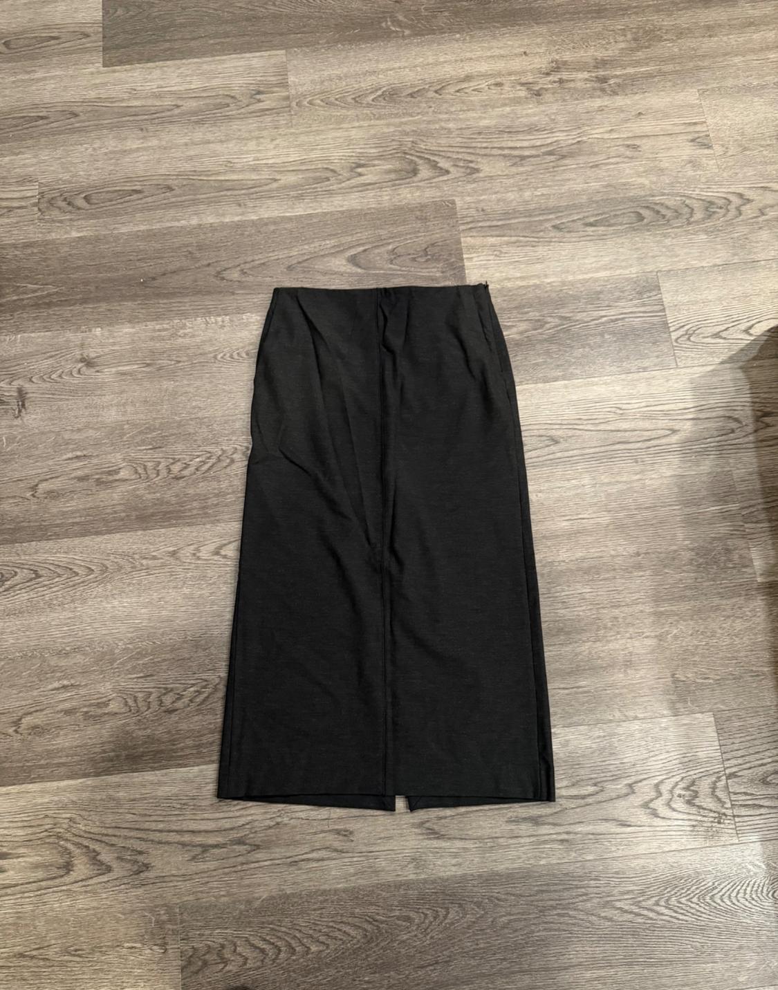 Black long skirt on light wood flooring with visible grain. The skirt has a simple and straight design.