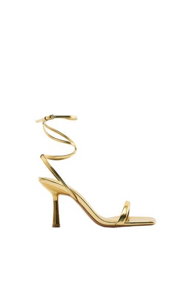 Side view of a gold high-heeled sandal with an ankle strap.