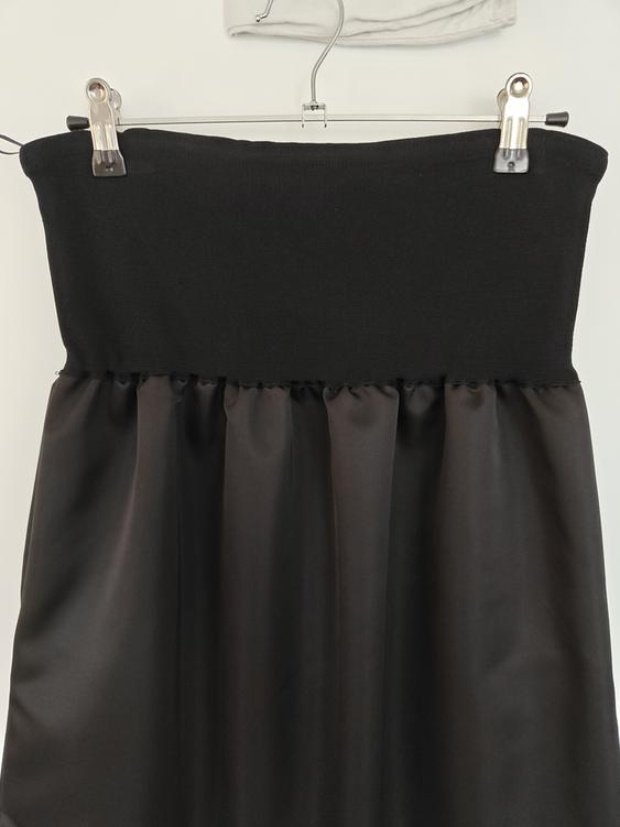 Black skirt hanging on a hanger with clips, elastic fabric top and satin fabric bottom. White background.