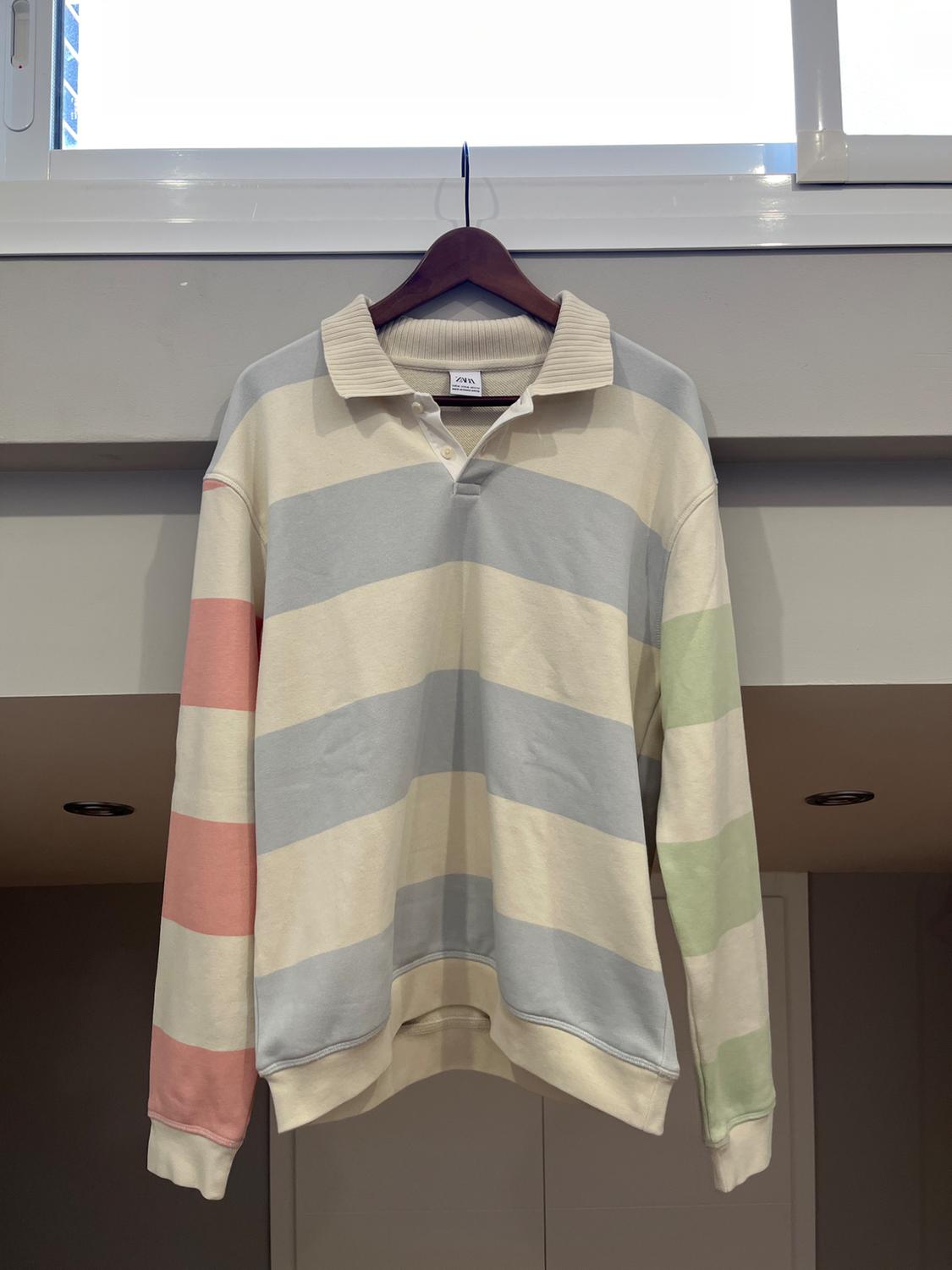 Wide striped pastel jumper hanging on a wooden hanger. Grey wall background and white window above.