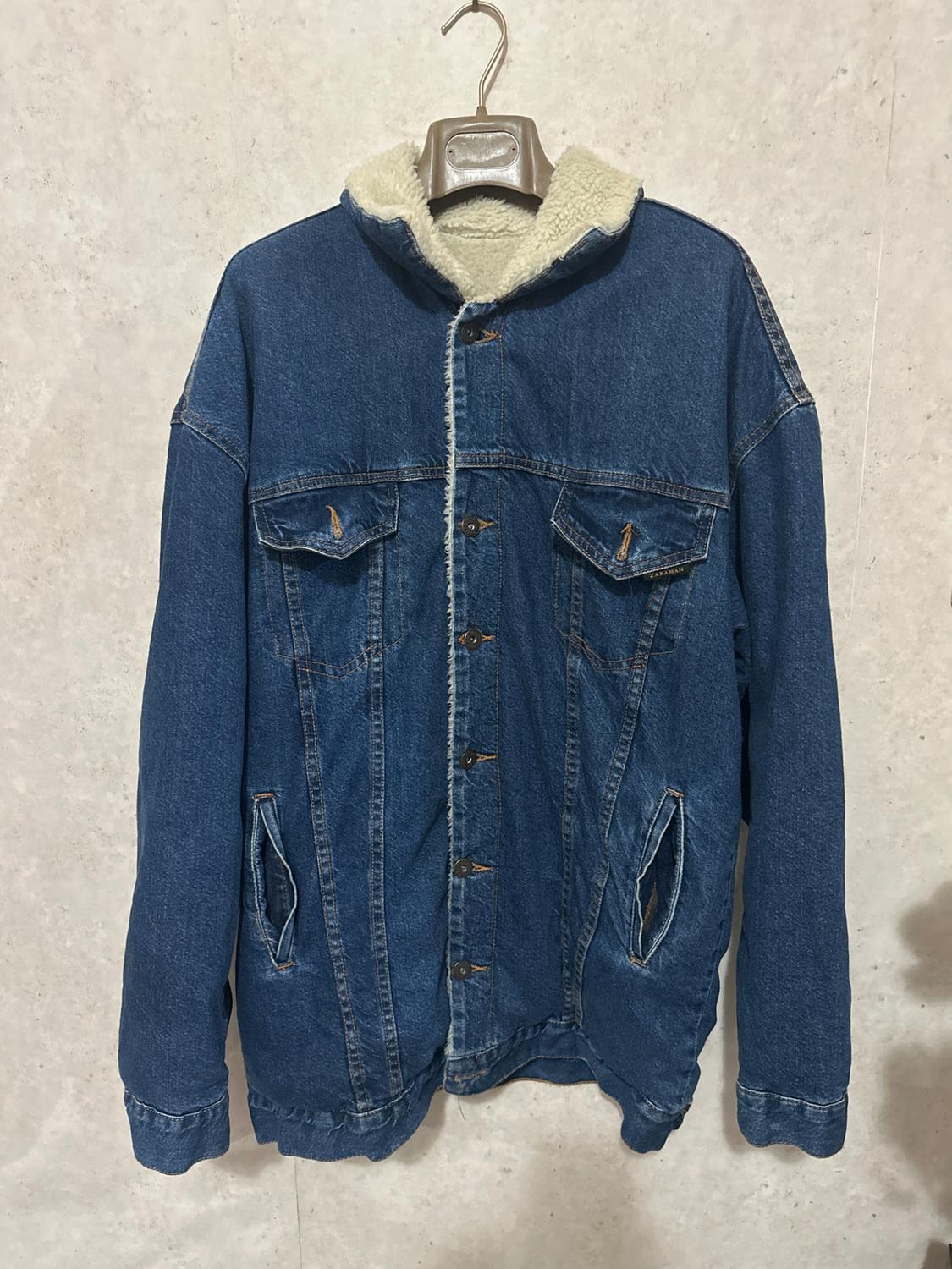 Blue denim jacket with a white fleece lining, hanging on a hanger against a light background.
